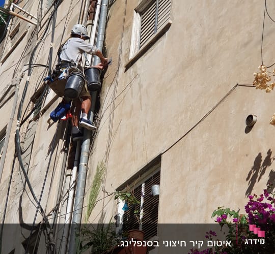 אדם מטפס על קיר עם ציוד עבודה בגובה